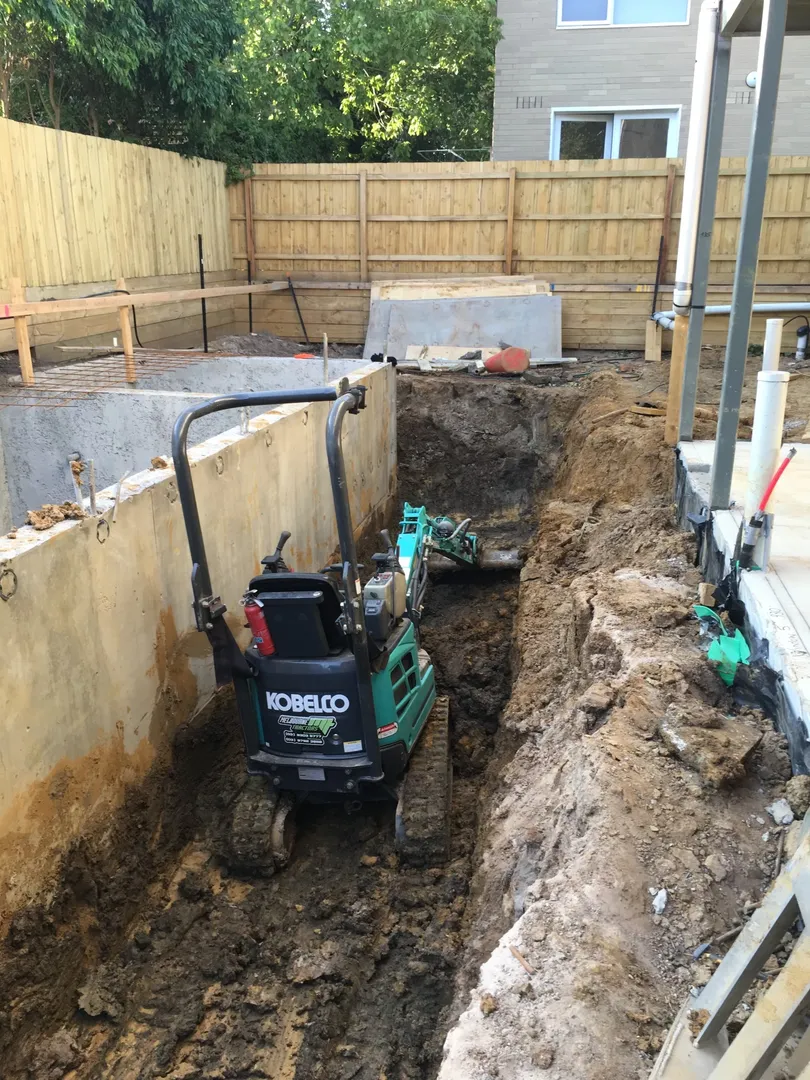 Mini excavator digging trench in residential backyard construction.