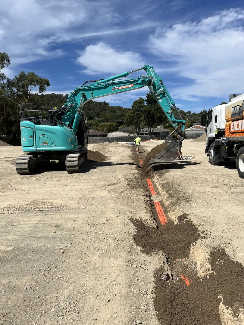 Excavator digging trench with orange markers, clear sky background.