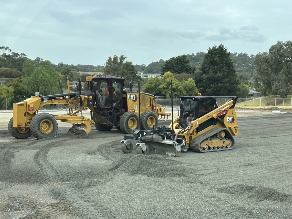 Construction vehicles grading gravel at a worksite.