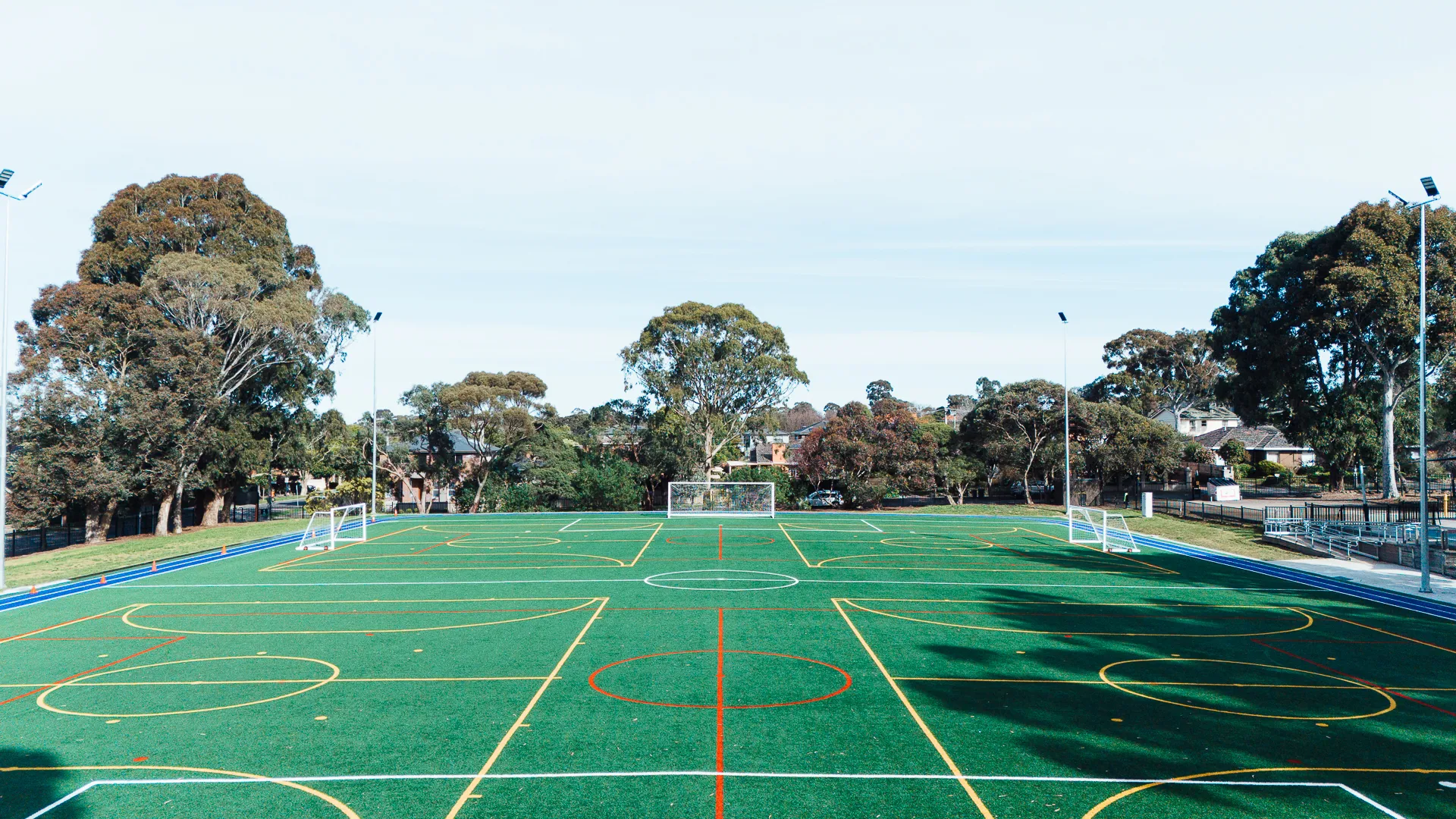 Empty outdoor soccer field amidst trees and houses.