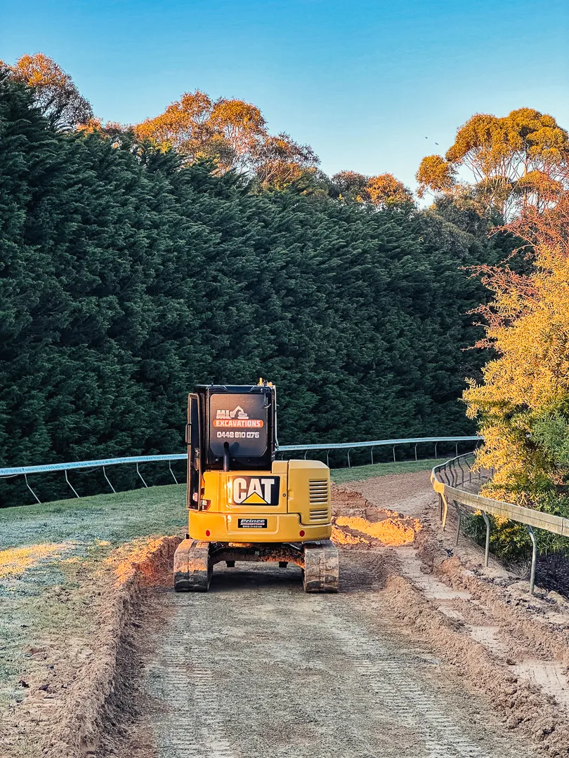 Excavator on dirt track amidst green forest.